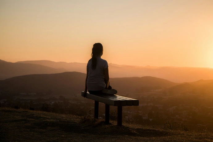 woman sitting on bench overlooking mountain